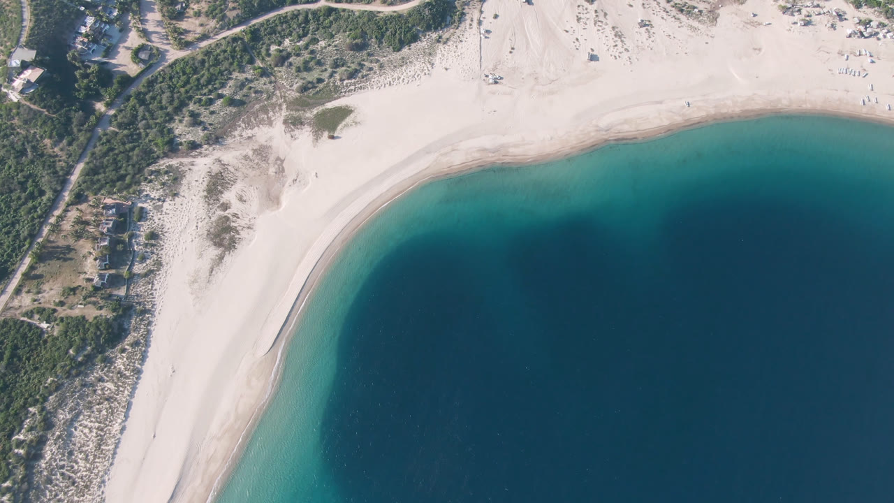Opening overhead frame of Los Frailes, Baja California Sur, showing pale sand curving around turquoise shallows and darker water, with no visible people.