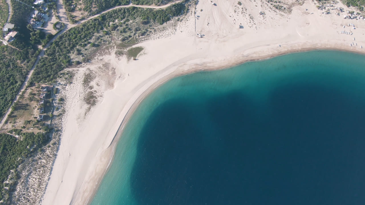 One second into the Los Frailes aerial view, the beach arc and teal nearshore band remain centered, with scrubland and roads above and no visible people.