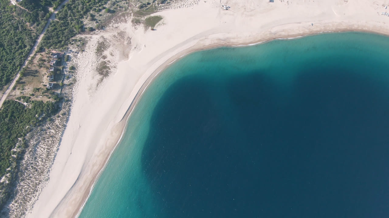 Overhead view of a curved sandy beach beside blue water and green coastal scrub.