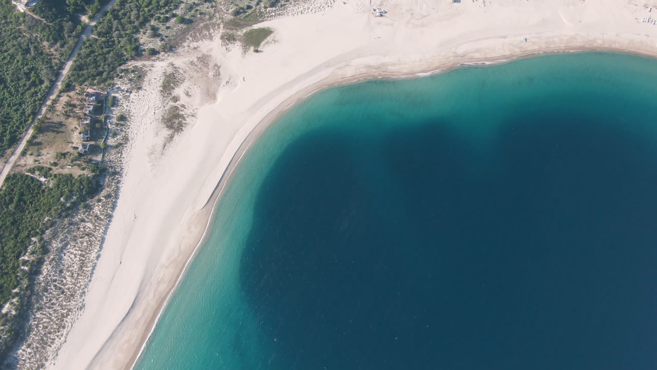 Aerial view at Los Frailes with the sandy shoreline running diagonally across the frame, clear shallow water near shore, darker water offshore, and no visible people.