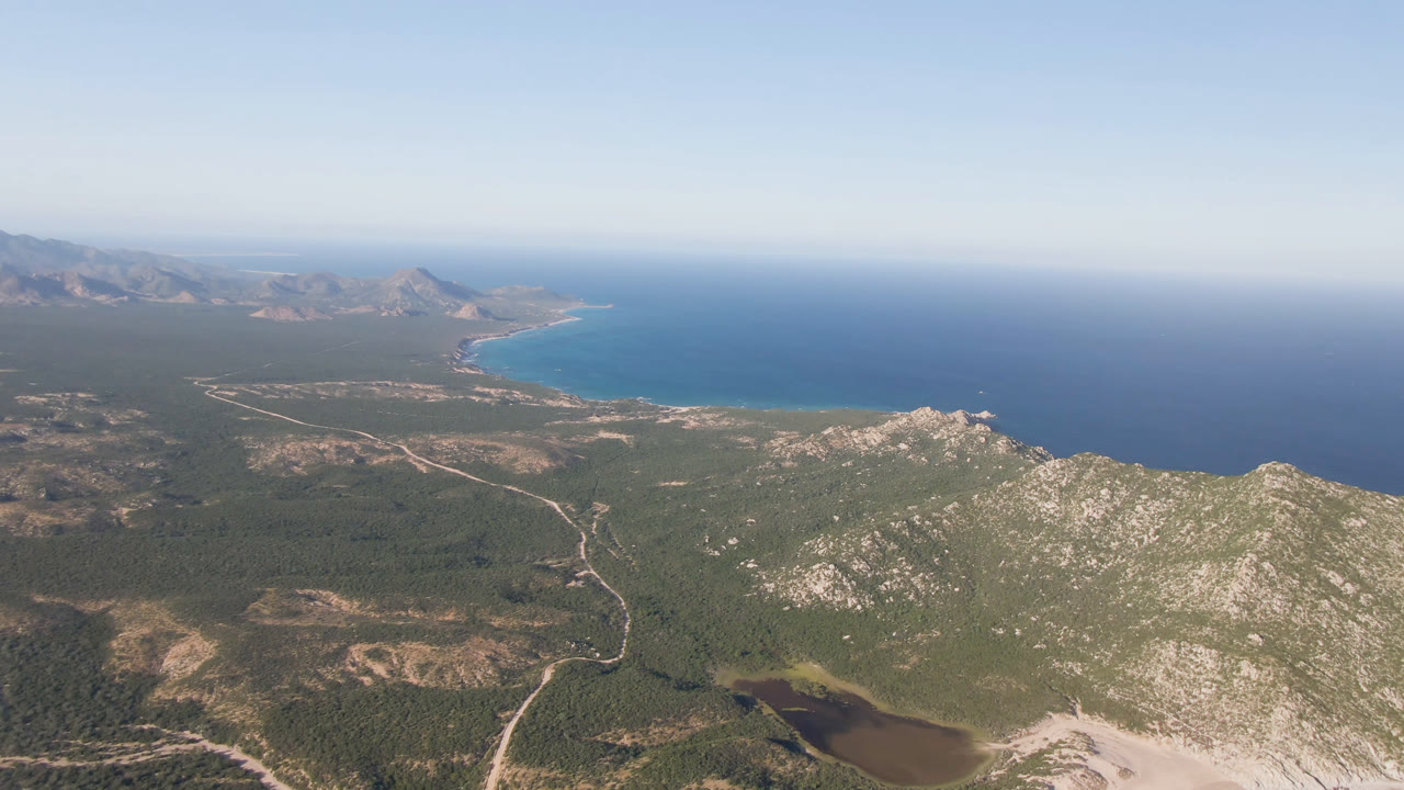 High aerial view of coastline, ocean, hills, roads, and a small dark lagoon.