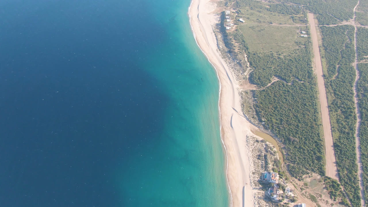 Top-down coastal view with ocean, beach, vegetation, and inland tracks.