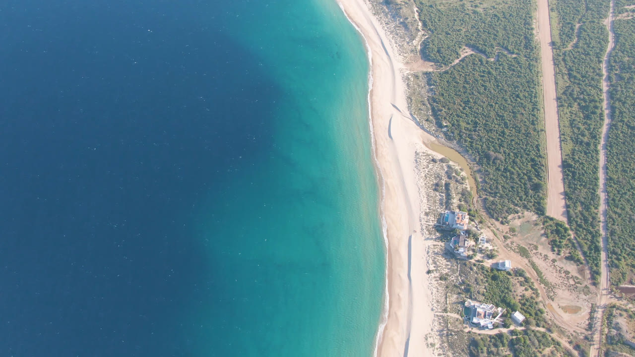 At 0:01, the Los Frailes aerial view holds on the curved beach and color gradient from dark ocean to shallow turquoise water, with scrubland, a road, buildings, and no visible people.
