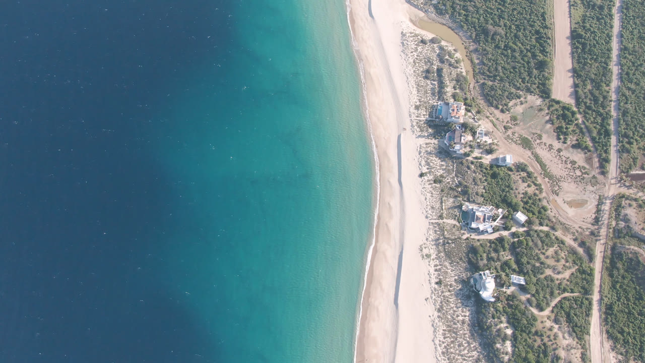 Top-down beach view with turquoise shallows and inland vegetation.
