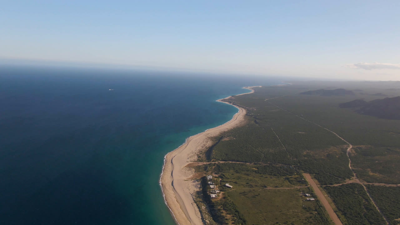 Aerial view of Los Frailes coastline with turquoise water near the shore, darker ocean offshore, a long sandy beach, inland dirt tracks, and no visible people.