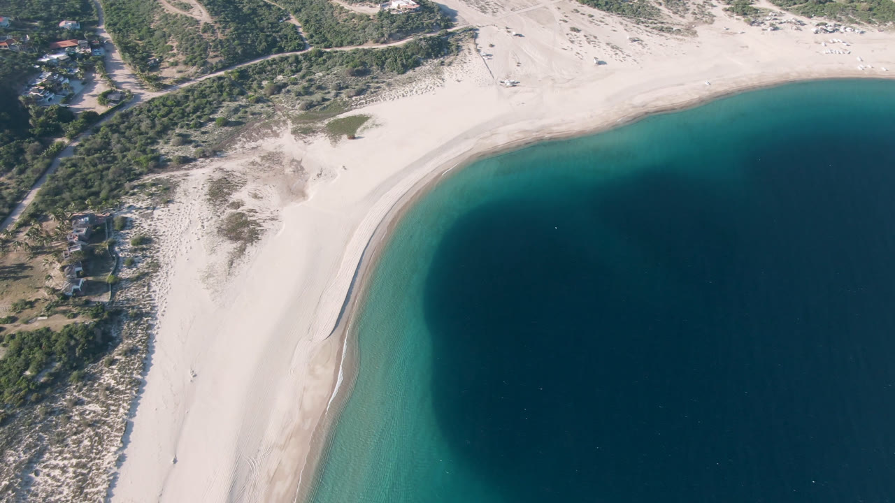 Drone view of sandy beach curving around dark blue water