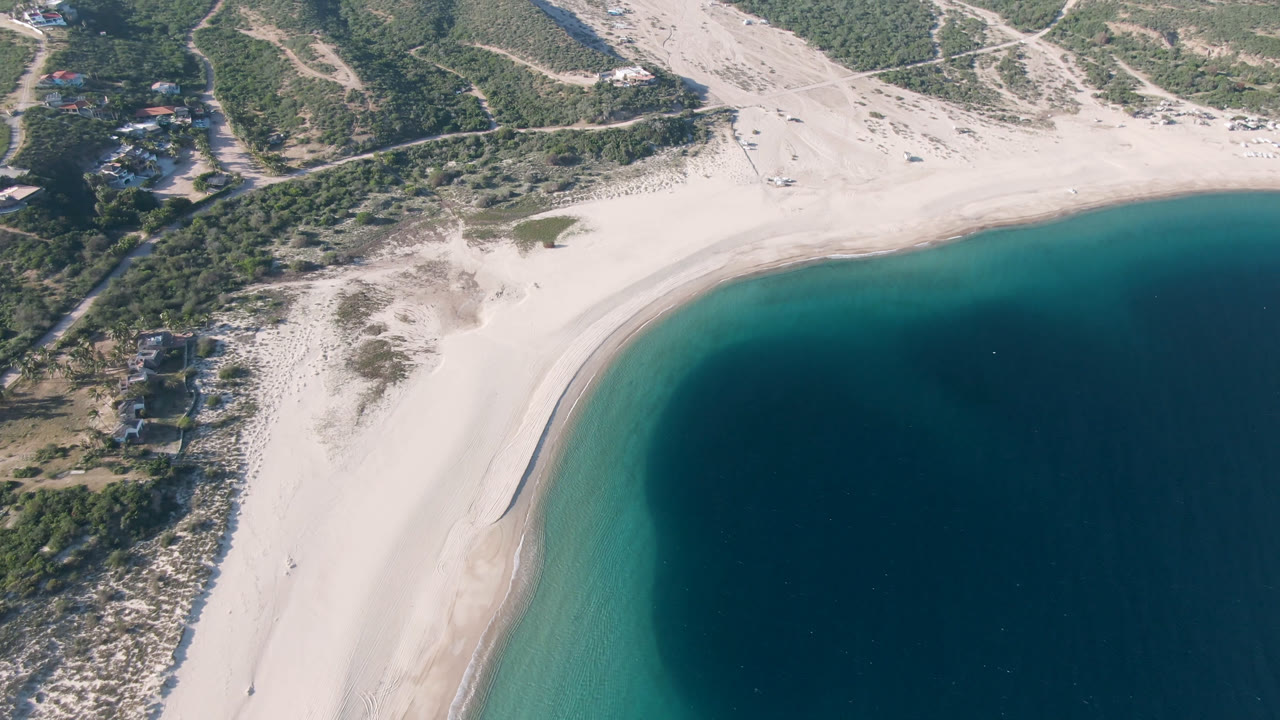 Aerial view of a curved sandy beach beside blue water and scrub hills.
