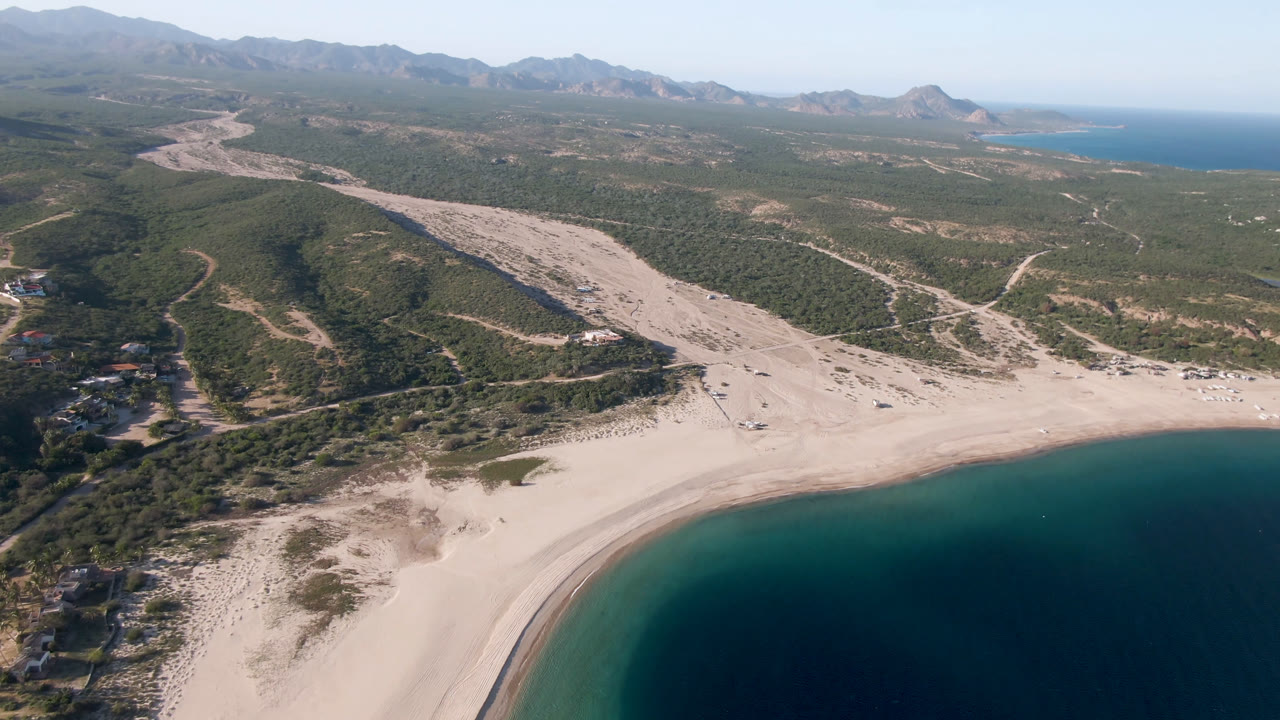Wide aerial coastline view with beach, water, valley washes, hills, and mountains.