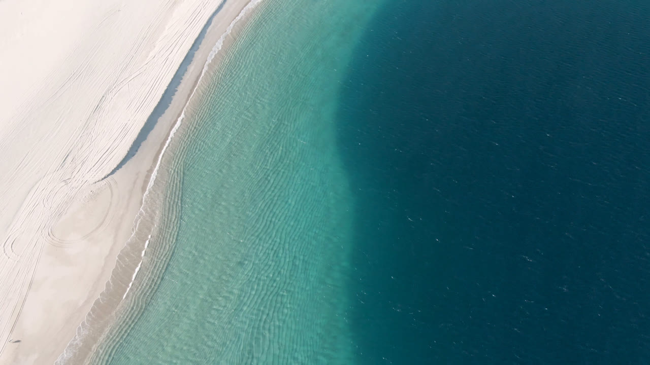Curved sandy shoreline meeting clear turquoise sea from above