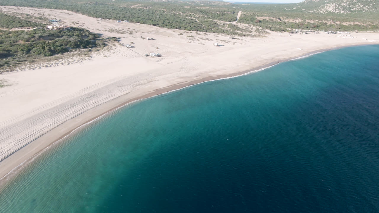 Wide aerial beach view with dark blue water in the foreground.
