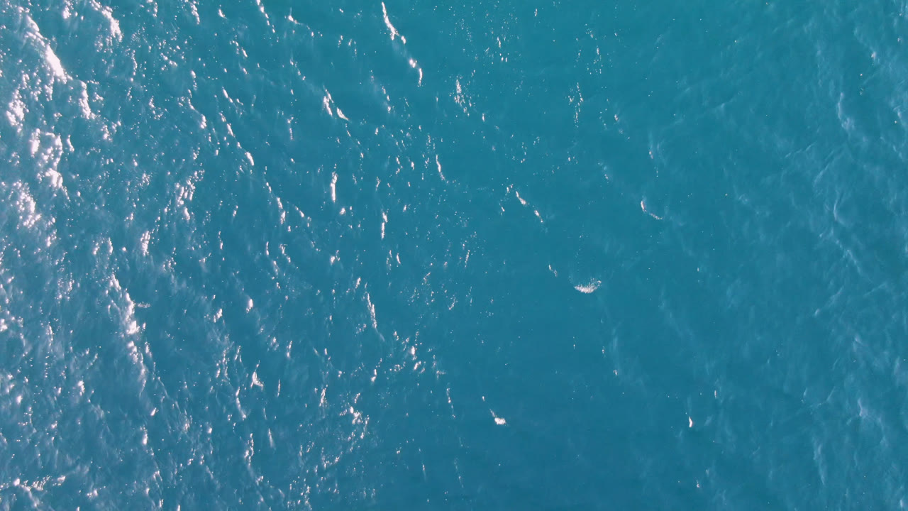 Top-down view of turquoise ocean water at Los Frailes, Baja California Sur, with bright sun flecks near the upper left and no visible people.
