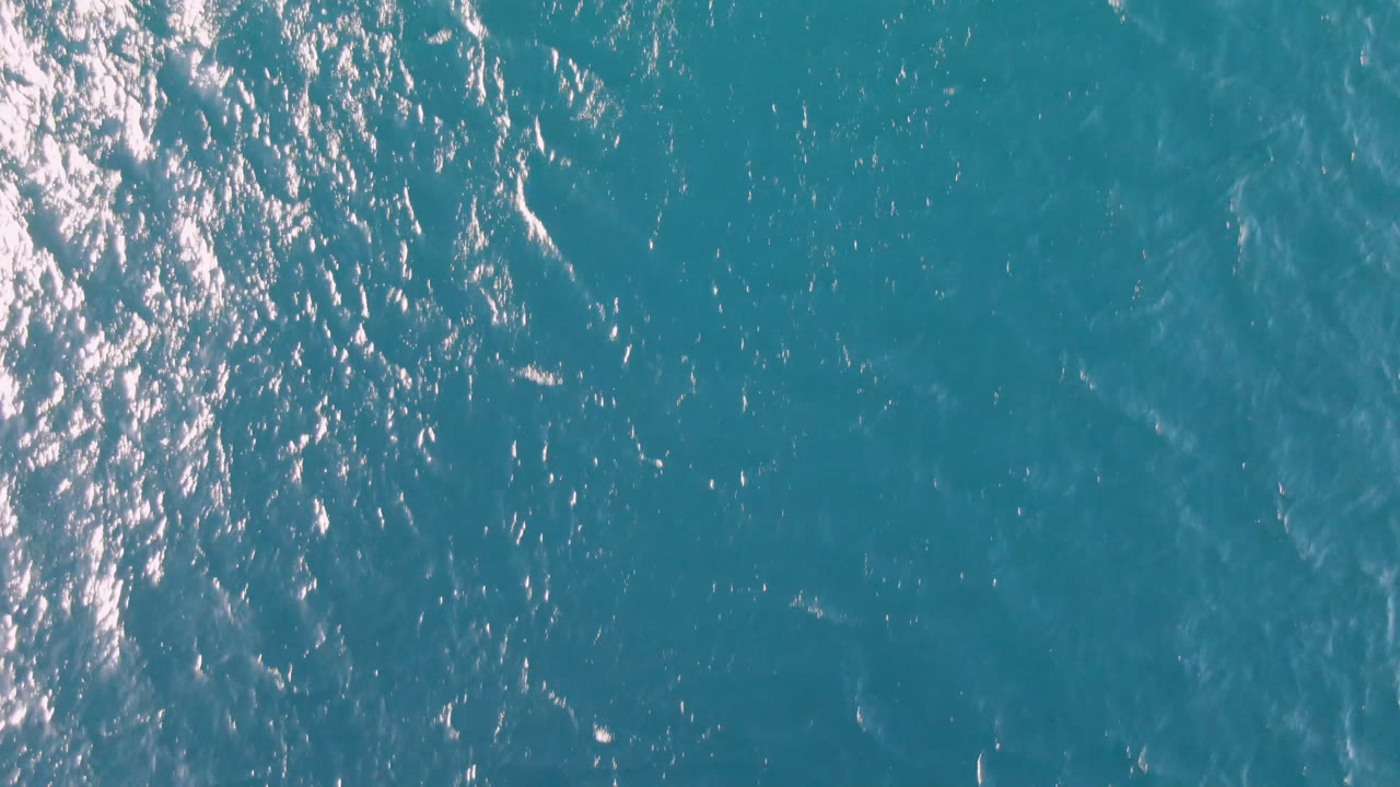 Teal ocean surface with shimmering highlights and faint wave lines.