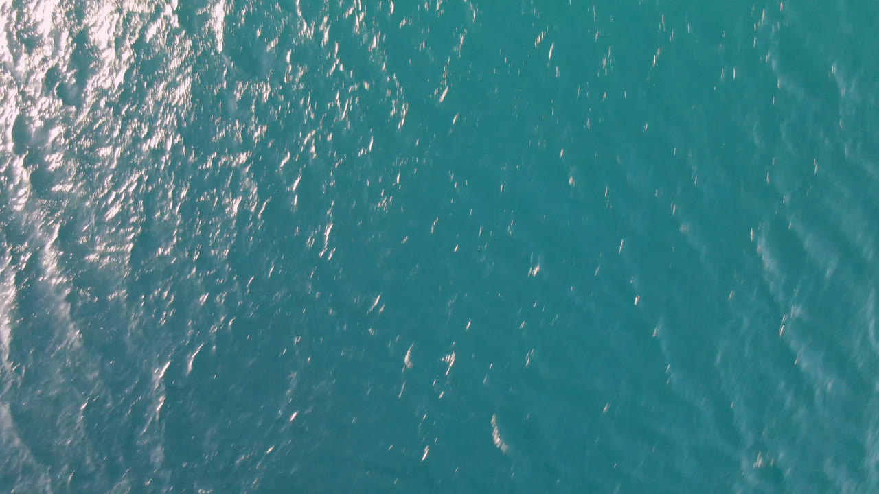Top-down view of teal ocean water in Los Frailes, Baja California Sur, with bright highlights clustered along the left side and no visible people.