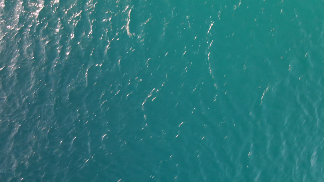 Teal ocean surface with scattered highlights and faint darker bands.