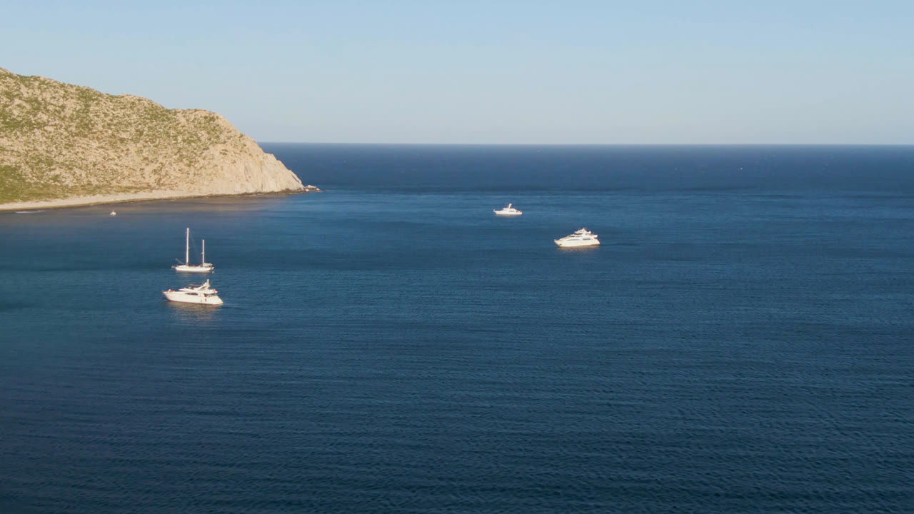 Boats floating on blue ocean near a rocky headland.