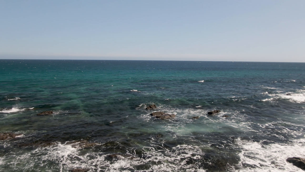 Wide ocean horizon above rocky surf and shallow turquoise water