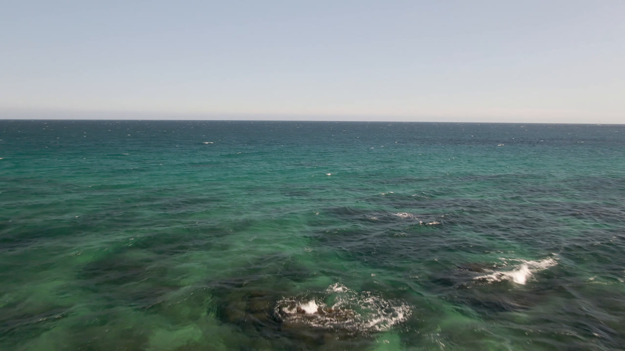 Open water at Shipwrecks Beach Los Cabos shows green-blue sea, scattered whitecaps, darker underwater patches, a level horizon, and no visible people.