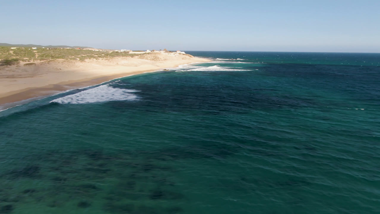 Shipwrecks Beach shoreline at 0:01, showing a curved band of sand, white foam pushing shoreward, dark patches in the water, and no visible people.
