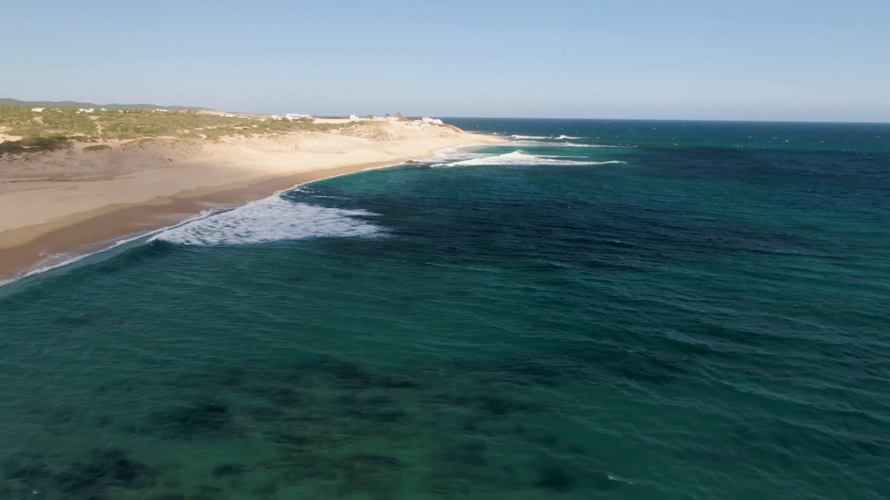 Wide aerial view of ocean water and surf meeting a pale beach.