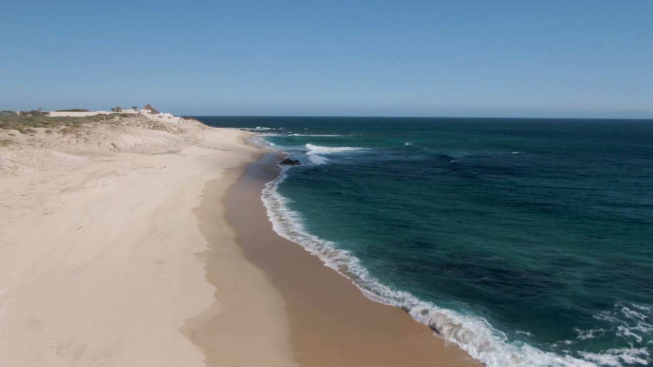 Aerial view of a sandy beach curving beside blue-green ocean water.