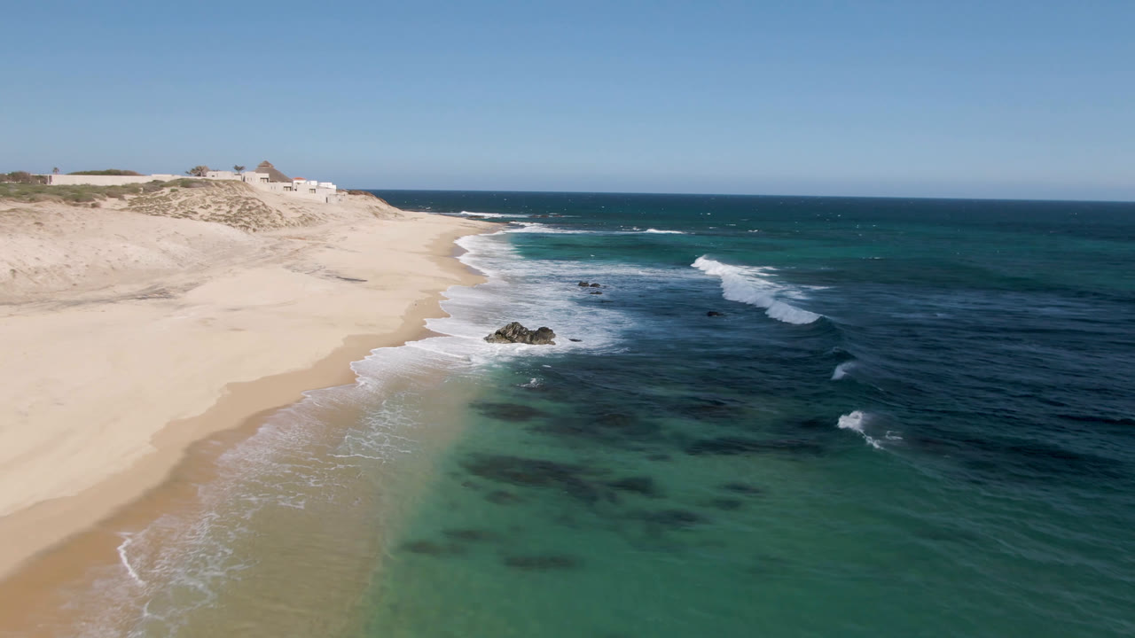 Aerial view of sandy beach, turquoise water, rocks, and breaking waves.