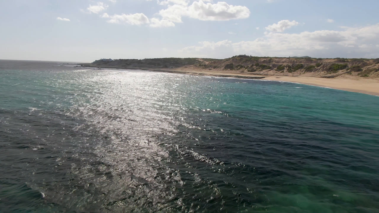 Bright ocean surface and turquoise shallows in front of a remote sandy beach.