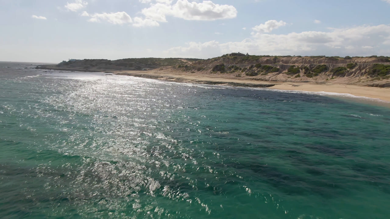 Green-blue coastal water with a sandy beach and rocky bluff line behind it.