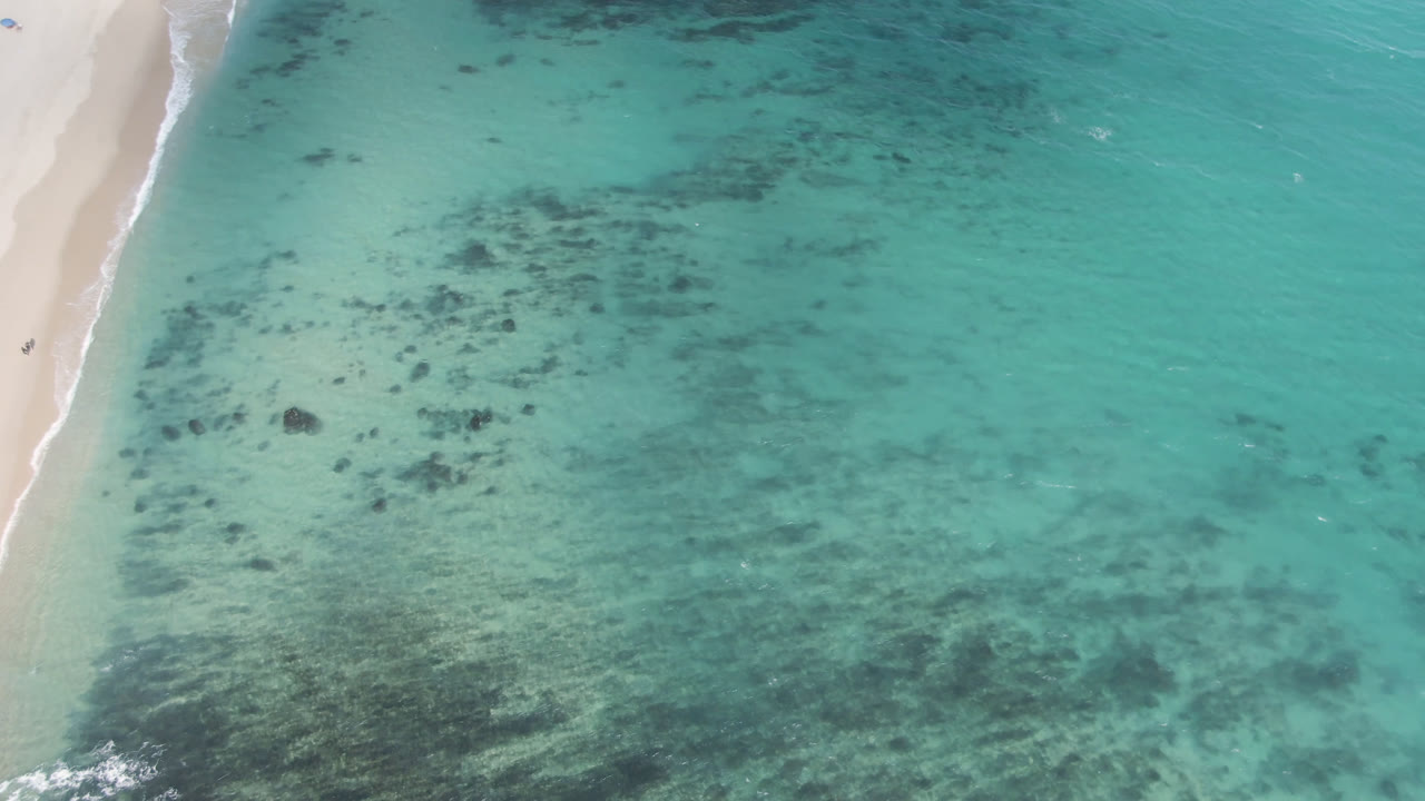 Overhead turquoise water beside a sandy beach with dark reef patches.