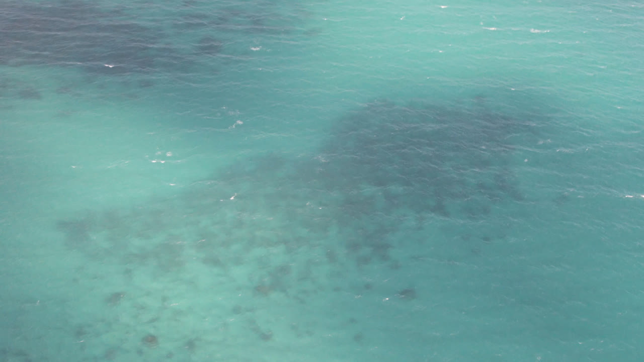 A slightly different patch of Shipwrecks Beach water shows pale turquoise surface, soft ripples, and dark shapes beneath with no visible people.