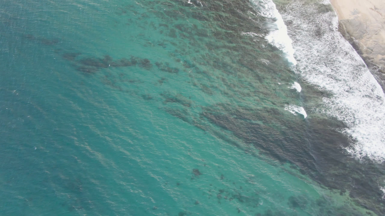 Overhead view of turquoise water at Shipwrecks Beach in Los Cabos, with white surf entering from the upper right and no visible people.