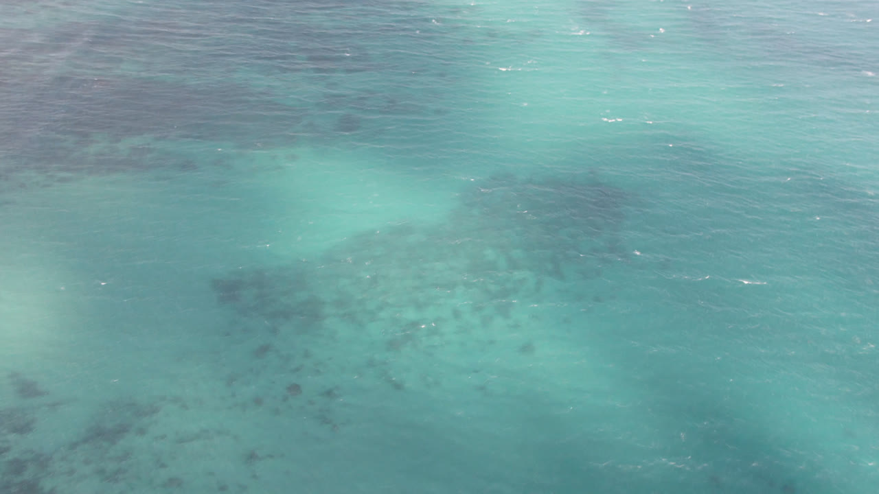 Overhead turquoise ocean with dark underwater patches and white surf near the top edge.