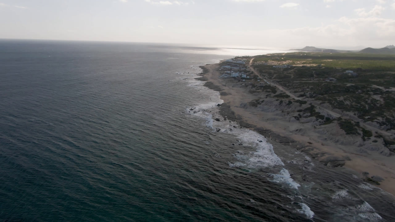 Wide coastal aerial with ocean, beach, scrubland, and horizon