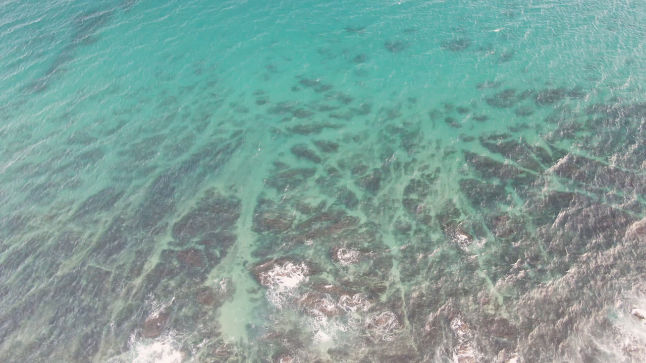 Turquoise sea surface with reef clusters and pale surf breaking near the bottom.