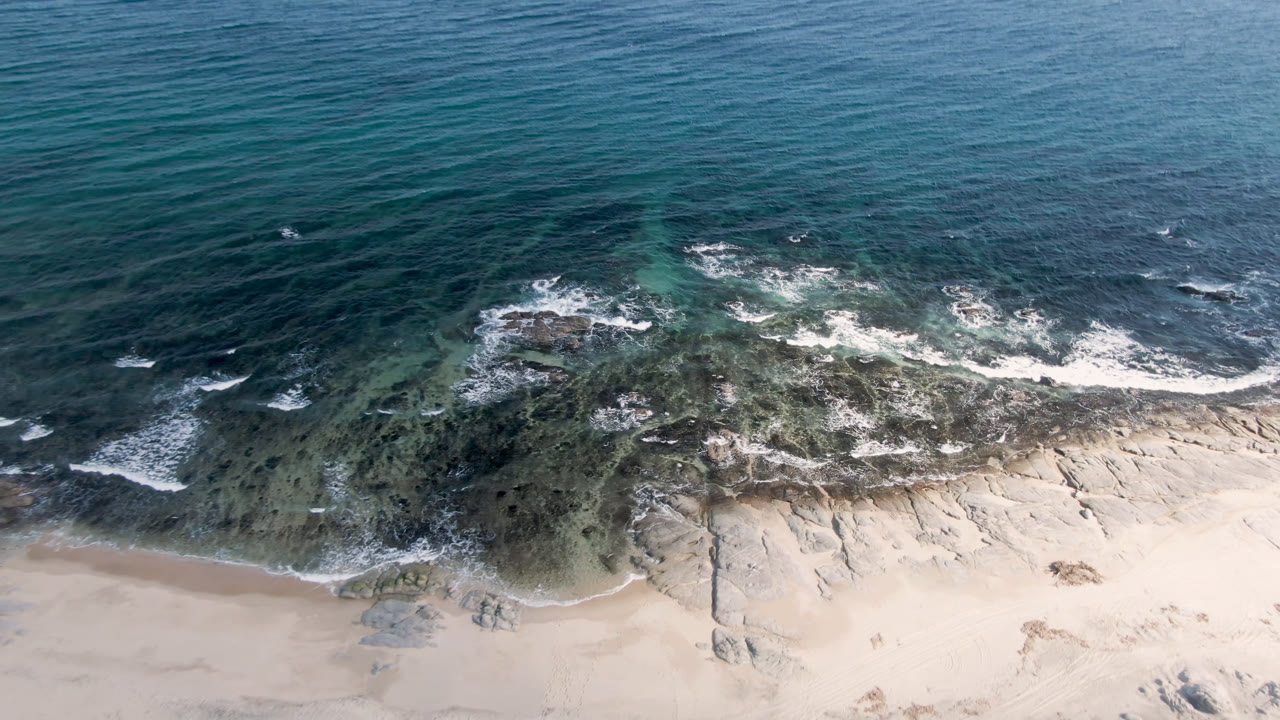 Drone view of turquoise water, reef patches, surf, and beach.