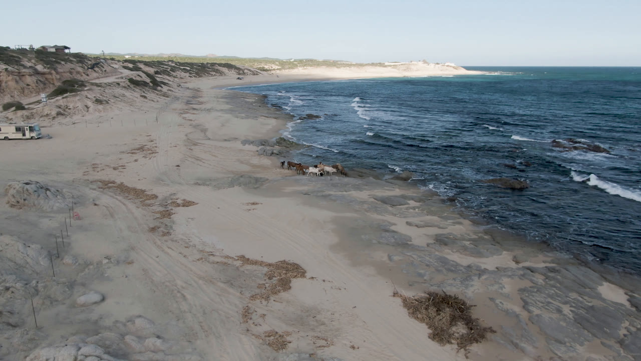 Elevated view of sandy beach, surf, rocks, and a small boat near the shoreline.