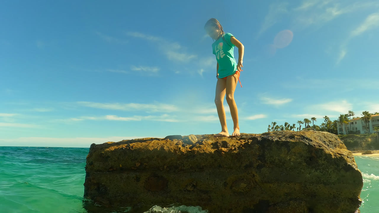 Girl standing on a rock above turquoise ocean water.