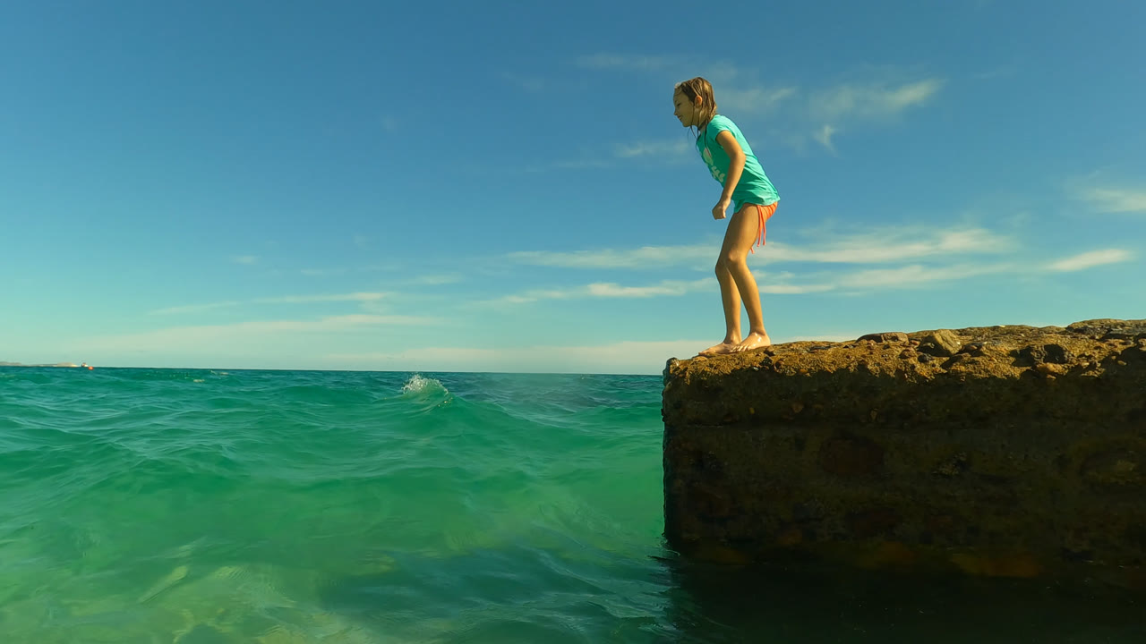 At San Jose Del Cabo, Mexico, the girl stands upright near the edge of the rock as small waves move across the turquoise water below.