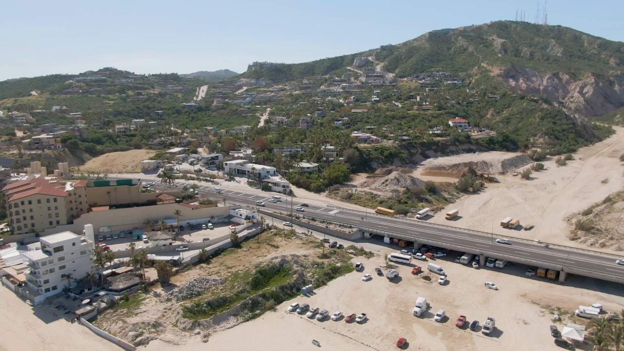 Aerial view of a highway bridge, sandy wash, hillside homes, and vehicles.