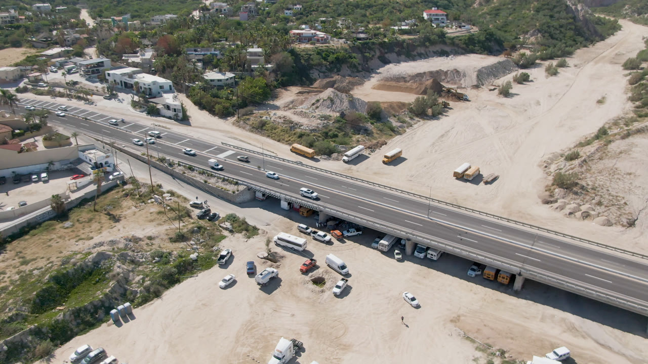 The 0:01 frame keeps the Costa Azul highway overpass centered, with cars spaced along the lanes, buses on the dirt roadside, hillside homes above, and no clearly visible people.