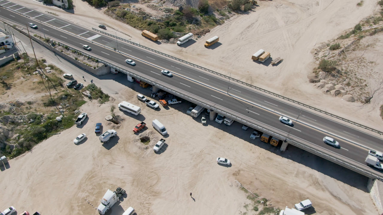 One second into the clip, the Costa Azul Los Cabos highway bridge remains centered with several cars spaced across the lanes, white vans parked below, and no clearly visible people.