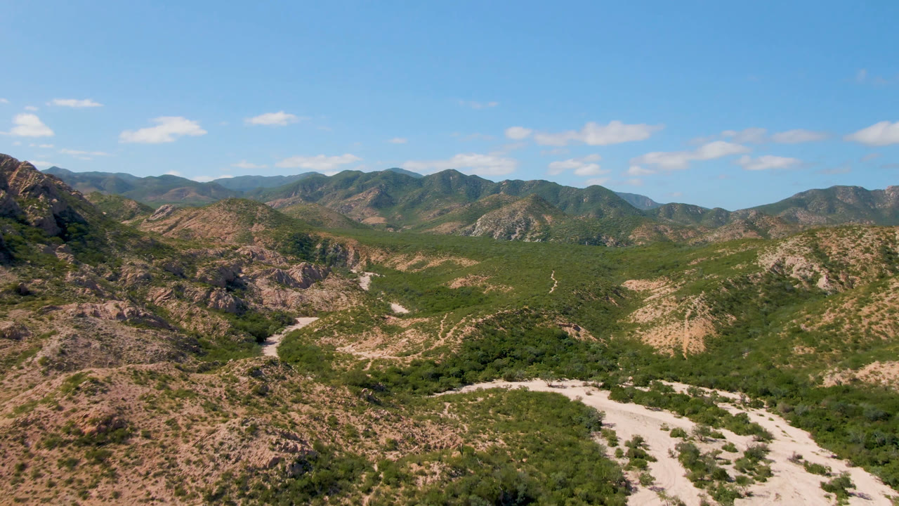 Wide aerial landscape of scrubby mountains and branching pale desert paths.