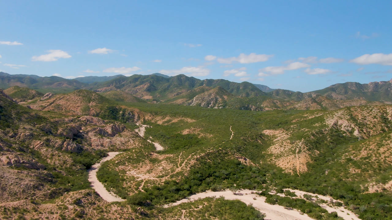 Opening frame of Cabo Pulmo, Baja California Sur, with a pale road curving through green valley growth below tan mountain ridges and no visible people.