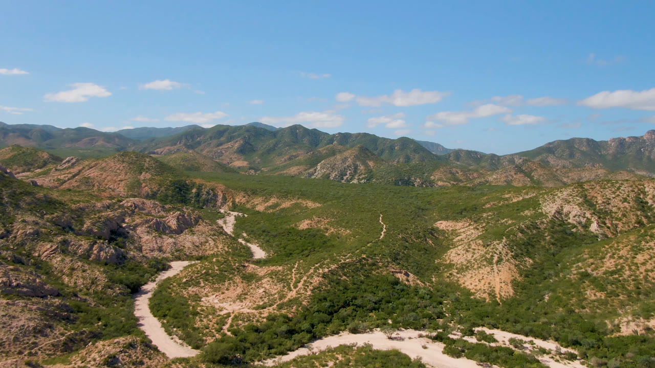 Cabo Pulmo aerial view showing scrubby green terrain across dry mountain slopes, a pale road in the valley, distant ridges, and no visible people.