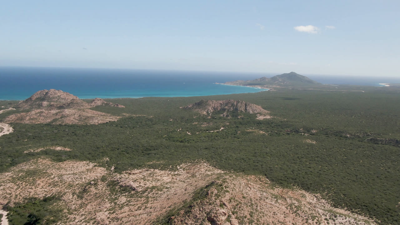 Wide aerial landscape with desert hills in front of a turquoise bay and open ocean.