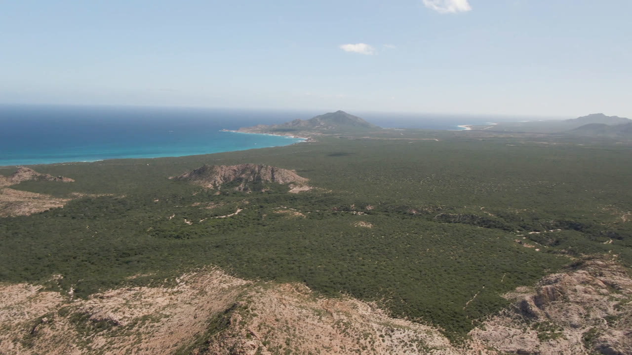 Aerial view of green coastal terrain, rocky ridges, mountains, and blue ocean.