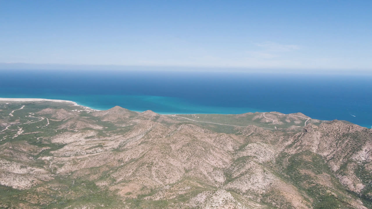 Aerial coastal landscape with low mountains, beach line, and open ocean.