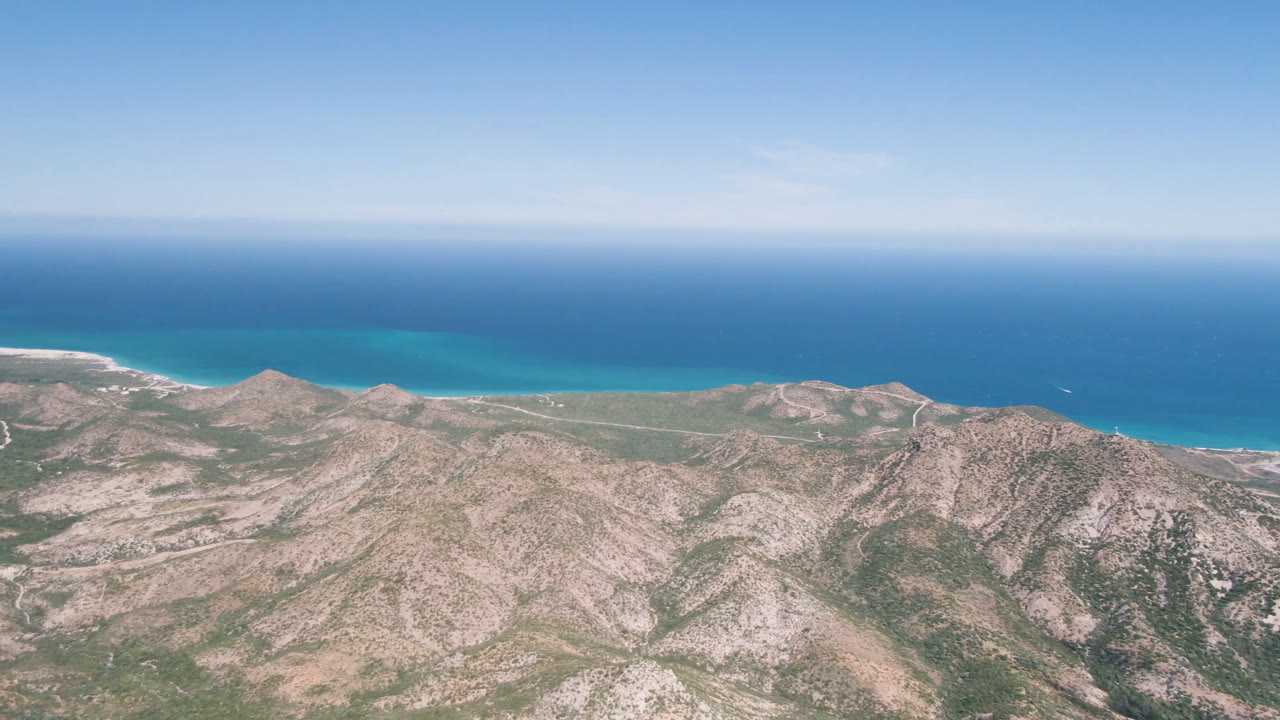 Rocky coastal mountains with blue ocean and clear sky beyond.