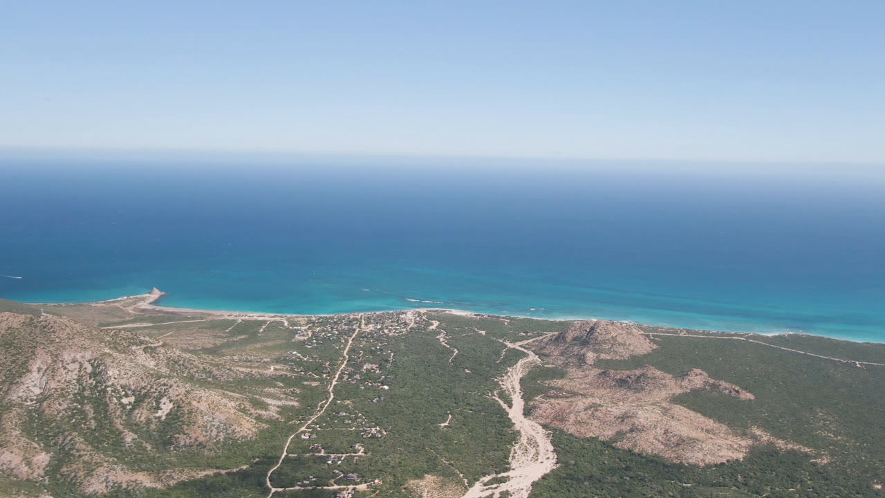 Aerial view of desert coastline with hills, beach, turquoise water, and horizon.