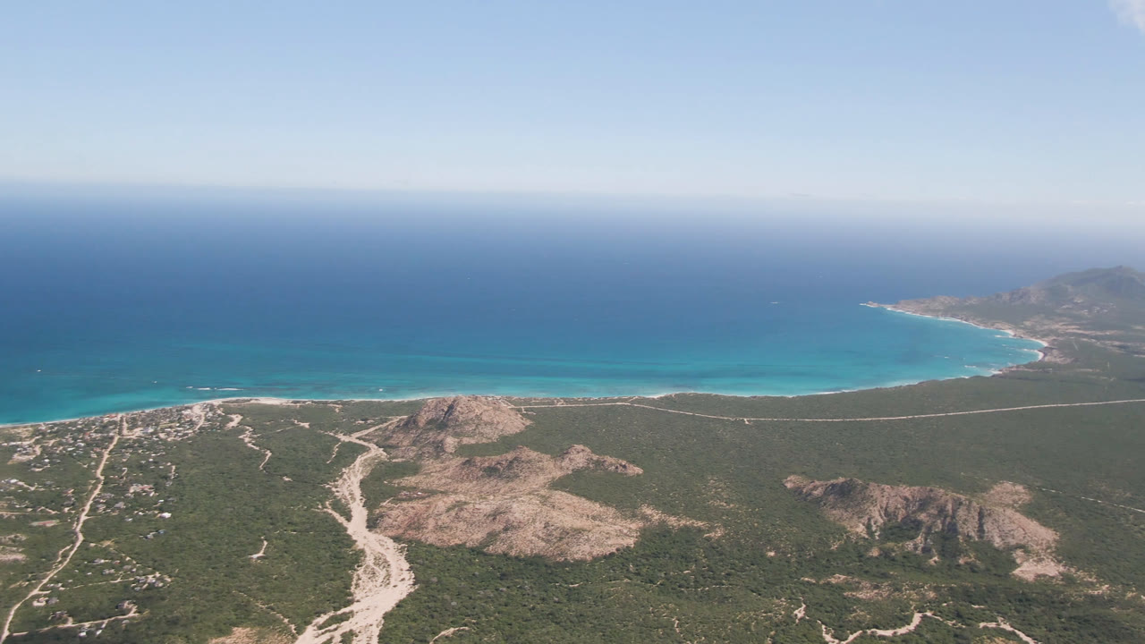 Coastal aerial with beach arc, ocean, desert hills, and distant point