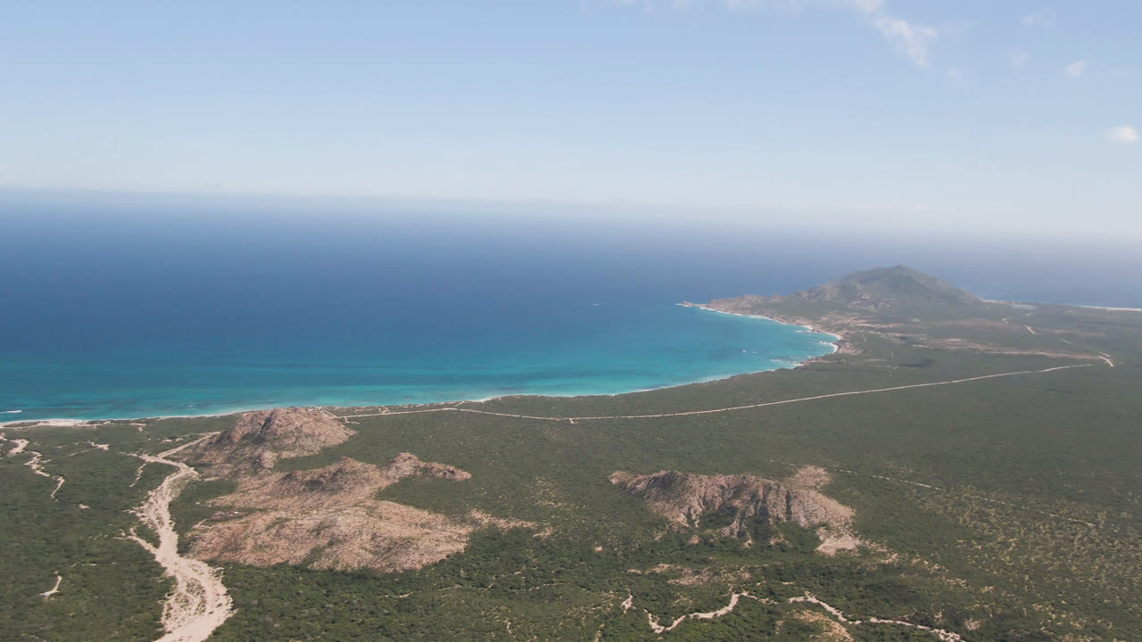 Aerial coastline with rocky foreground, beach, blue ocean, and distant headland